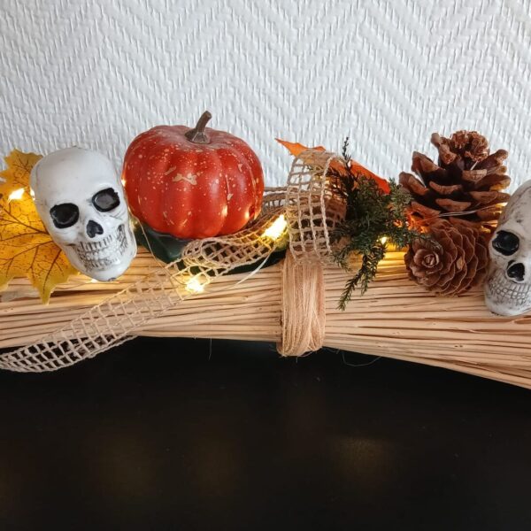 Décoration d’Halloween lumineuse sur un fagot de paille, ornée de deux crânes, d’une citrouille, d’araignées et de pommes de pin.