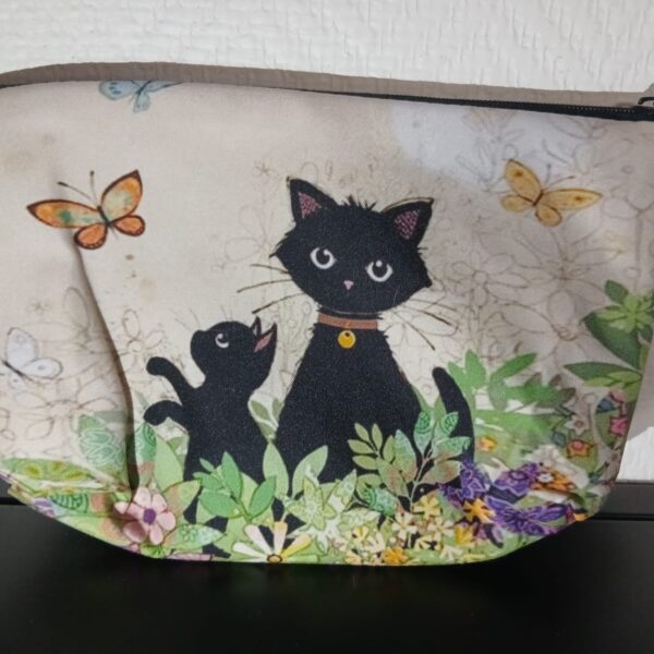 Pochette beige à fermeture zippée, illustrée de deux chats noirs entourés de fleurs et de papillons.