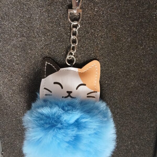 Porte-clés représentant une tête de chat tricolore, surmontée d’un pompon bleu en fausse fourrure.